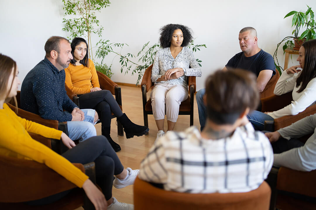 Group of mixed race and gendered people in sitting in a circle for a group therapy session.